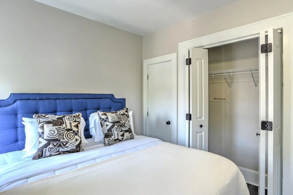 A close-up view of a bed with a plush blue upholstered headboard, decorative pillows, and crisp white bedding. The scene is styled simply but elegantly, with an emphasis on comfort and serenity.