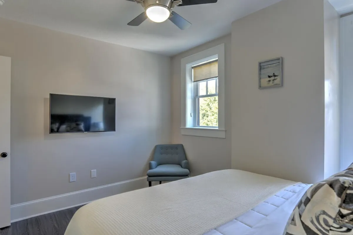 This image shows a serene interior space featuring a neatly made bed, a nearby television, a window with treetop views, and an accent chair inviting relaxation. The natural light streaming through the window hints at the elevated vantage point of the third-floor setting, while the arrangement of furniture conveys a calm and inviting atmosphere.